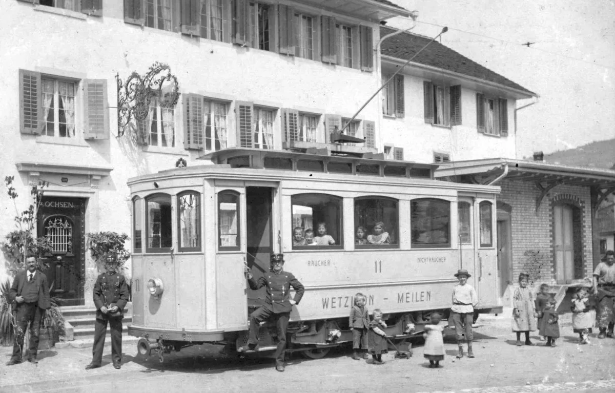 Man sieht einen Triebwagen der Wetzikon-Meilen-Bahn mit Zugpersonal und Kindern.